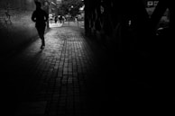 A silhouette of a man in a sharp blazer walking through an urban alley at dusk, city lights glowing behind.