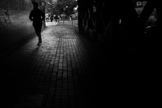 A silhouette of a man in a sharp blazer walking through an urban alley at dusk, city lights glowing behind.