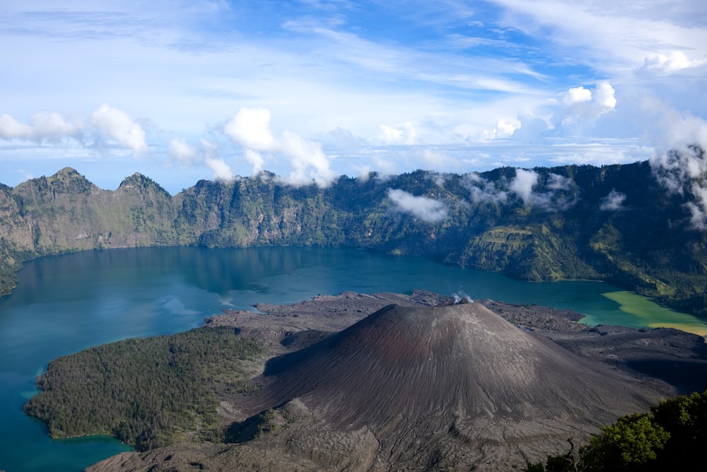 brown and green mountain surrounded by calm water at daytime