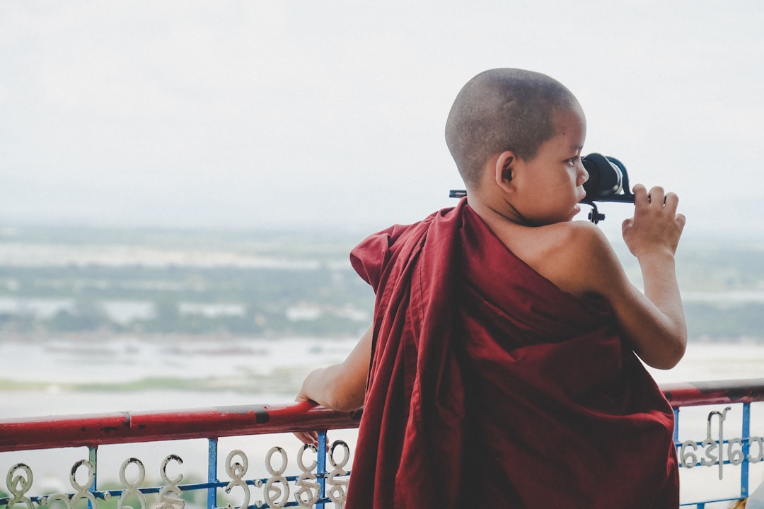 boy in red apparel leaning on blue and red metal railing during daytime