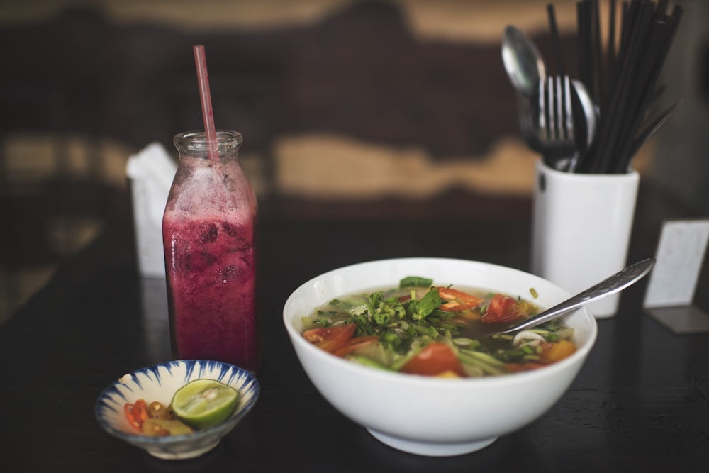 bowl of soup on black surface near bottle filled with pink liquid