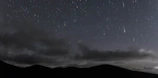 Night sky filled with shooting stars over mountains.