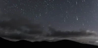 A night sky illuminated by a bright shooting star streaking over rolling hills.