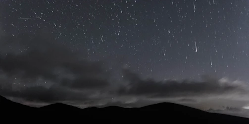 Night sky filled with shooting stars over mountains.