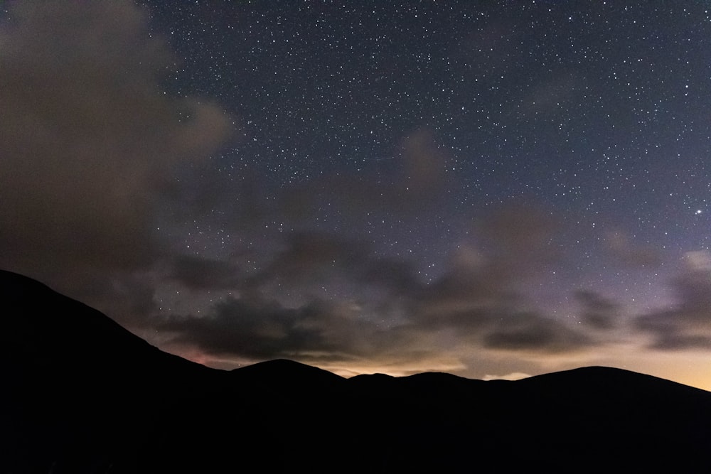 silhueta da montanha sob o céu estrelado ao pôr do sol