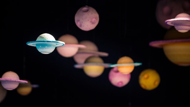 A collection of colorful, spherical objects resembling planets suspended against a dark background. Each sphere has unique colors and patterns, with some featuring rings similar to Saturn.