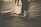 Sepia-toned photograph of a person's legs and feet extended, with the person seated on a covered chair. The background appears blurred. The image focuses on the feet and lower legs, with the shoes tied tightly.