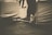 Sepia-toned photograph of a person's legs and feet extended, with the person seated on a covered chair. The background appears blurred. The image focuses on the feet and lower legs, with the shoes tied tightly.