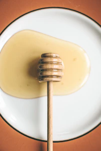 Close-up of golden macadamia honey dripping from a wooden honey dipper with macadamia tree blossoms in the background.