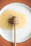 Close-up of a honey dipper dripping golden honey over a rustic wooden bowl surrounded by fresh herbs.