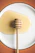 Close-up of a golden honey dipper dripping thick honey against a soft cream background.