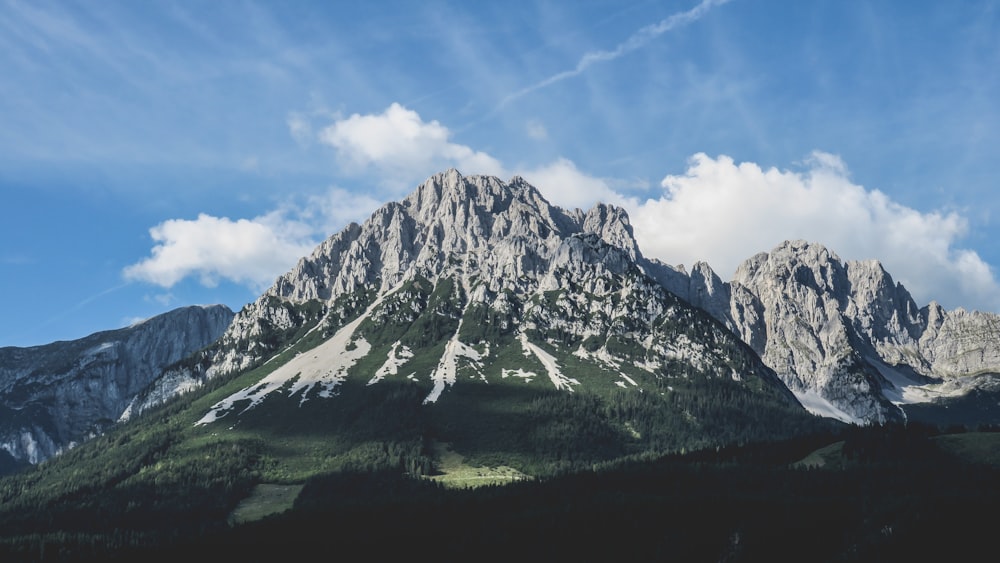 forest below rocky mountain under clouds