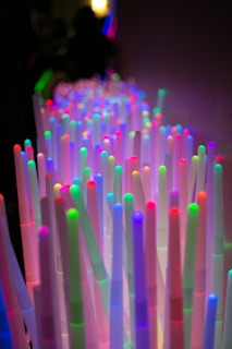 An array of upright, colorful LED light sticks, each glowing with vibrant hues of red, green, blue, purple, and pink, creating a mesmerizing visual effect in a dimly lit setting.