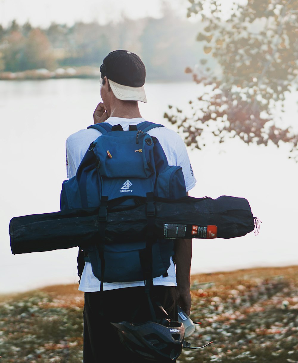 man wearing hiking backpack and tent bag standing near calm body of water