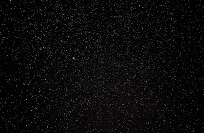 A vast expanse of a night sky filled with countless tiny stars scattered across a deep black background, with a single noticeably brighter star. The scene embodies the vastness of the universe.