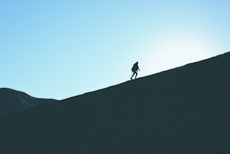 A determined young person climbing a steep hill at sunrise, symbolizing grit and persistence.