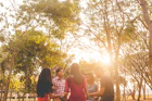 A diverse group of people holding hands in a circle during an outdoor prayer meeting, bathed in warm sunlight.