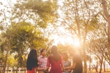 A small group sitting in a circle outdoors, sharing a warm conversation under soft green trees.