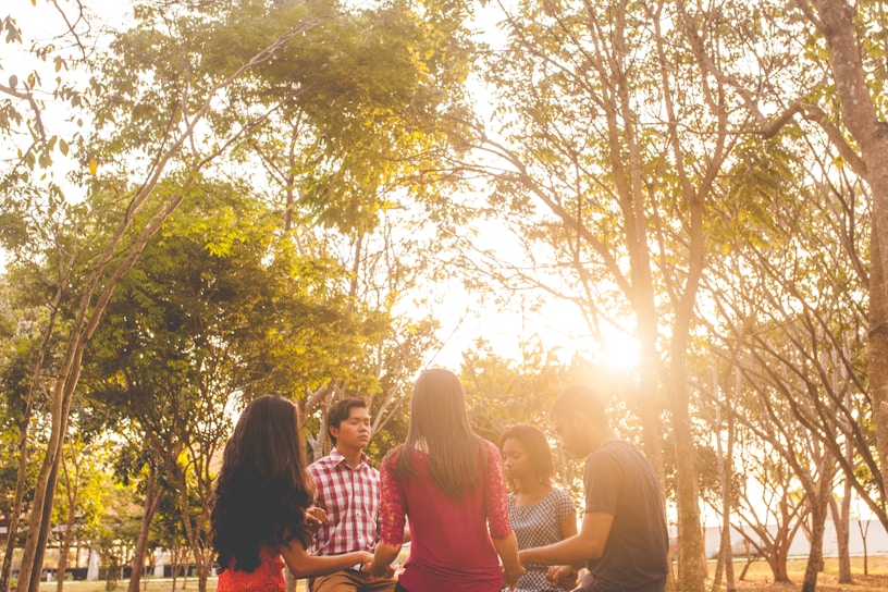 A joyful youth minister leading a small group discussion outdoors, sunlight filtering through trees.