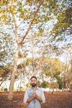 man with eyes closed and clasped hands in front of chest under green tree