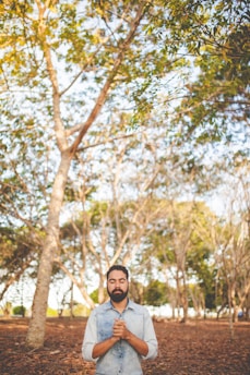 man with eyes closed and clasped hands in front of chest under green tree