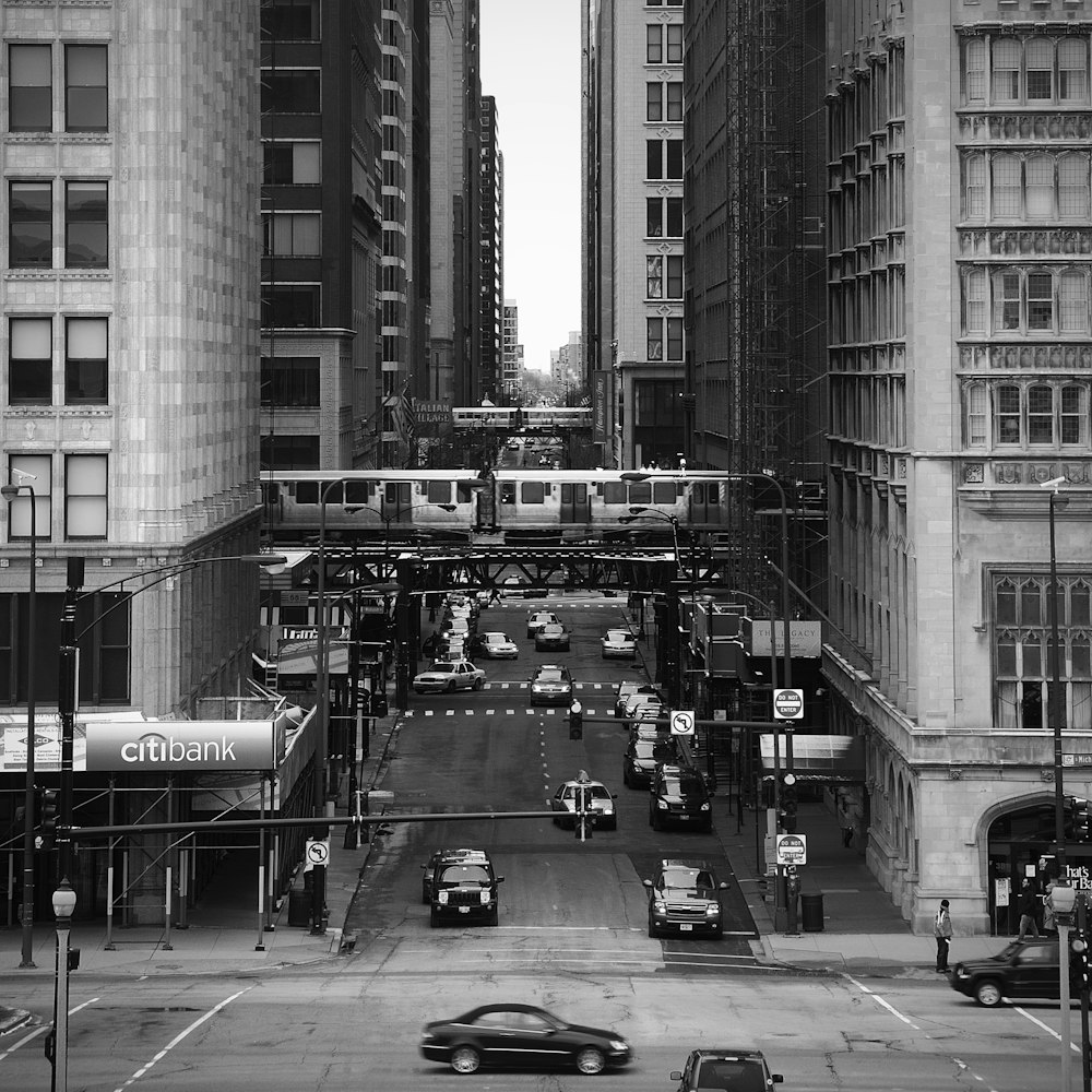 grayscale photography of vehicles between high rise buildings