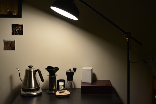Close-up of a minimalist desk setup with warm lighting, a sleek lamp, and a cup of coffee beside an open notebook.