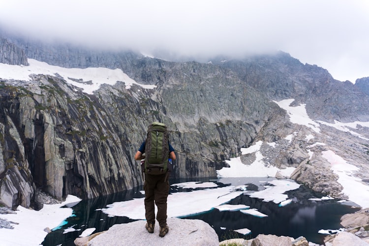 Hiker standing on a rock above an icy mountain lake, fog obscuring the mountaintops