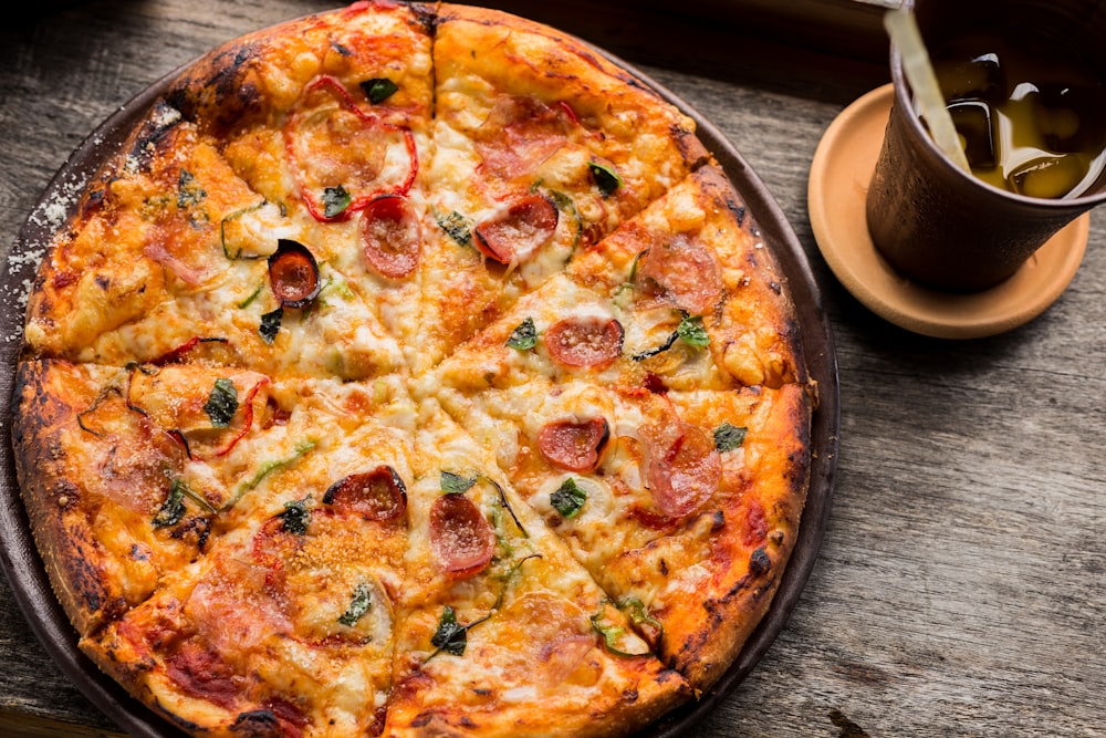 Photo de dessus de la pizza au pepperoni à côté d’une tasse brune remplie de liquide jaune et de glaçons