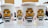 Four white beverage cups with illustrations of a yellow cartoon character wearing a striped outfit and goggles are placed closely together on a table. The cups have branding for 'Despicable Me 3' and are marked with a Coca-Cola logo. The background is blurred, with hints of a room and people.