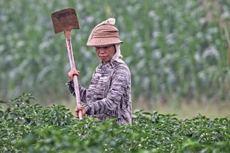 A friendly landscaper smiling while holding gardening tools in a lush green garden.