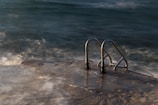 Stainless steel handrails leading into the ocean, with waves gently crashing against a concrete platform. The scene is captured during twilight, adding a mysterious and serene ambiance.