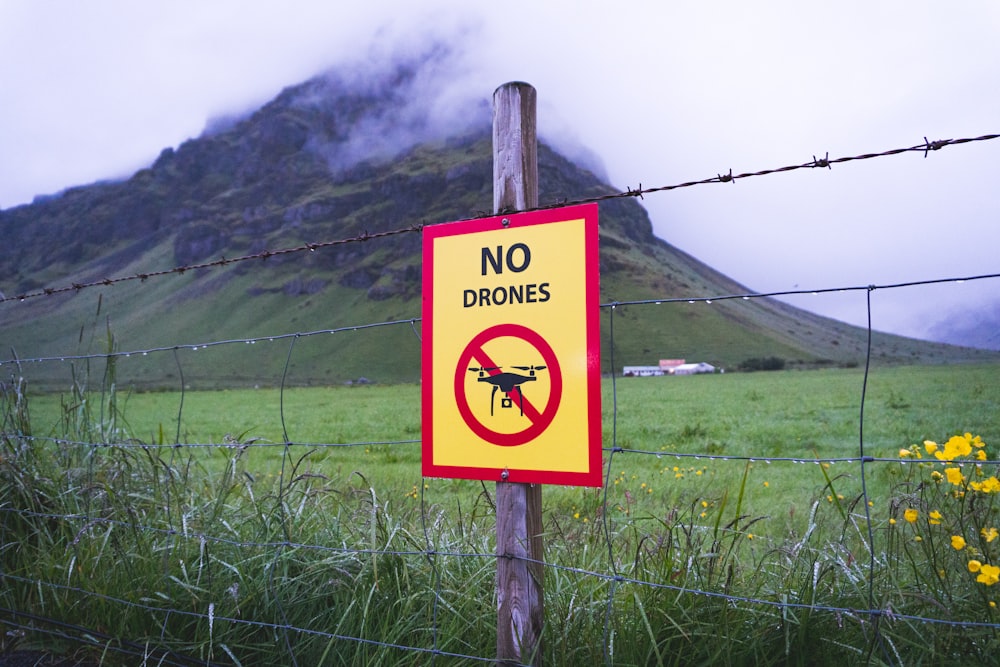 no drones signage on brown wooden post across mountain with fogs