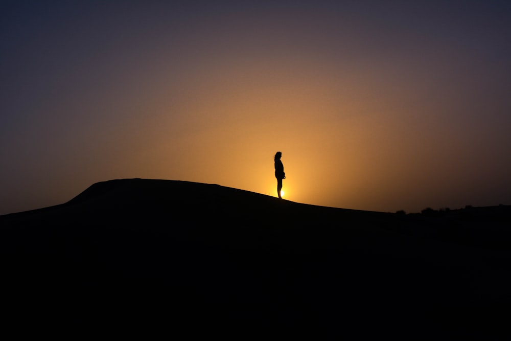 夕焼けの太陽と山の上に立つ人のシルエット