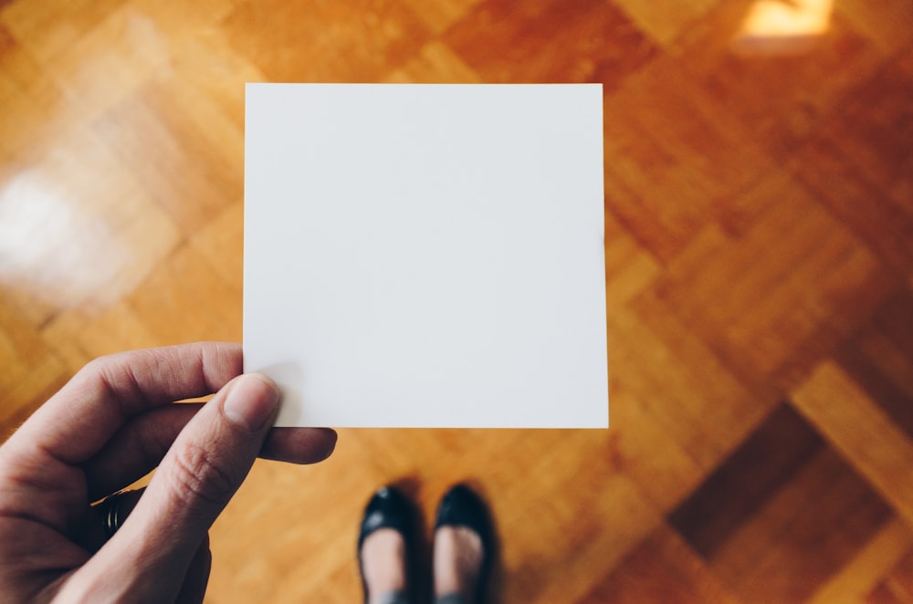 personne tenant du papier blanc sur un plancher en bois brun