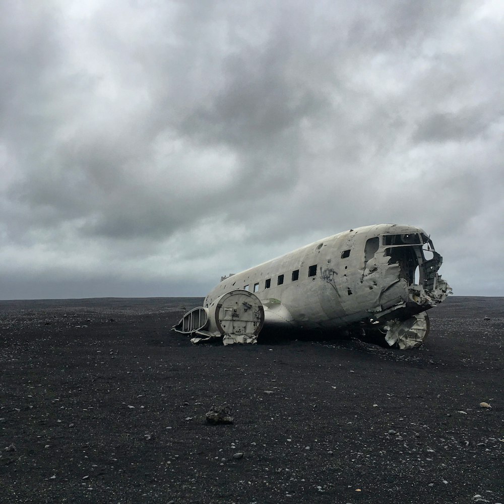 Avião cinza destruído em solo marrom sob nuvens cinzentas durante o dia