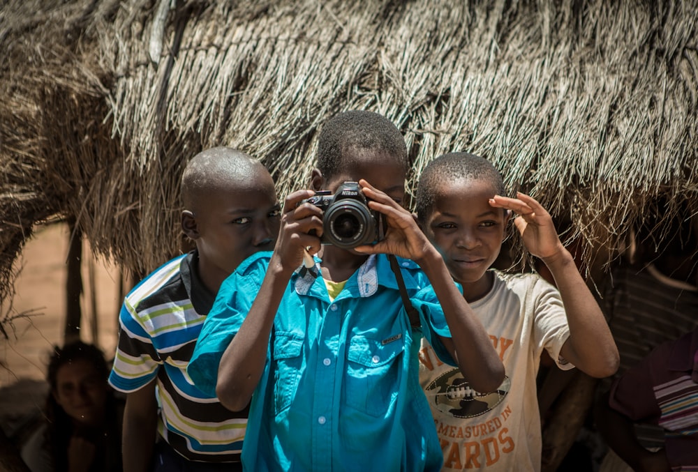 two boys standing behind boy using camera