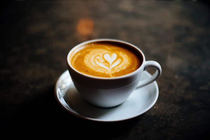 A cappuccino with latte art on a saucer over a dark stone table
