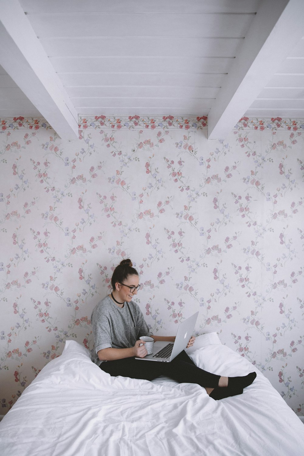 woman holding white ceramic cup while using laptop