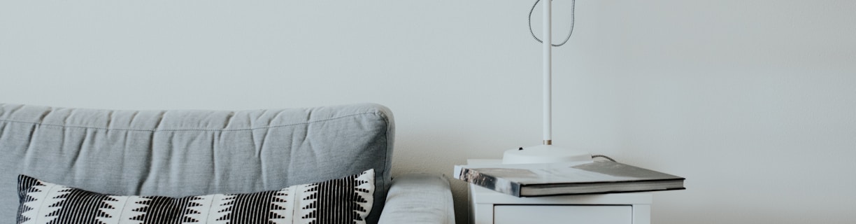 white study lamp on top of white wooden end table beside gray fabric sofa