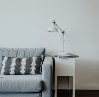 white study lamp on top of white wooden end table beside gray fabric sofa