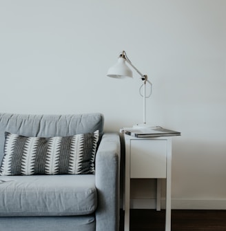 white study lamp on top of white wooden end table beside gray fabric sofa