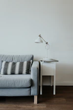 white study lamp on top of white wooden end table beside gray fabric sofa