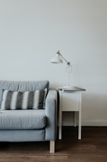 white study lamp on top of white wooden end table beside gray fabric sofa