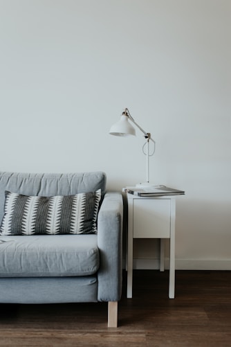 white study lamp on top of white wooden end table beside gray fabric sofa