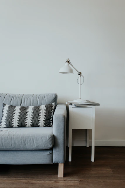 white study lamp on top of white wooden end table beside gray fabric sofa