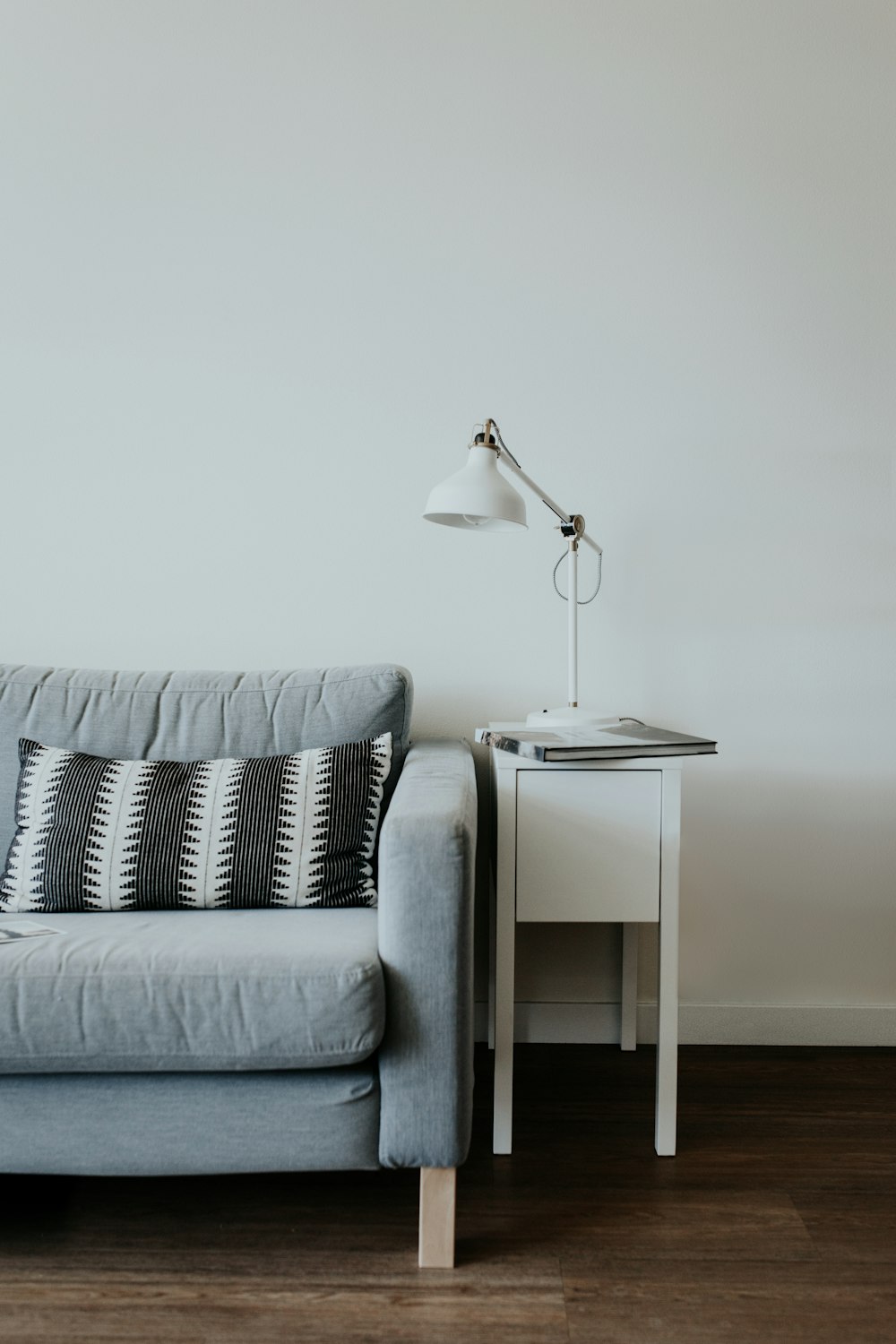 lampada da studio bianca sopra il tavolino in legno bianco accanto al divano in tessuto grigio