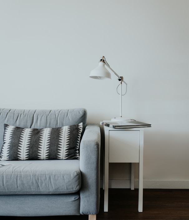 white study lamp on top of white wooden end table beside gray fabric sofa