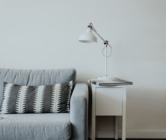 white study lamp on top of white wooden end table beside gray fabric sofa