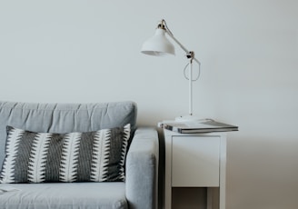 white study lamp on top of white wooden end table beside gray fabric sofa